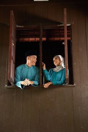 malay young couple at the wooden window of a traditional malay houseの写真素材