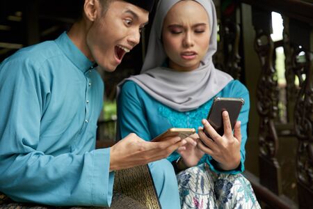 Muslim couple in traditional Malay clothing sitting at wooden stair during Eid al-Fitr celebration.の写真素材