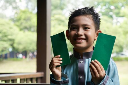 malay boy in a Malay traditional costume showing his happy face after receiving money pocket during Hari Raya celebrationの写真素材