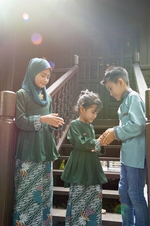 kids in traditional clothing , greeting in front of traditional malay house  during Hari Raya celebration.の写真素材