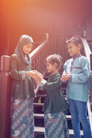 kids in traditional clothing , greeting in front of traditional malay house  during Hari Raya celebration.の写真素材