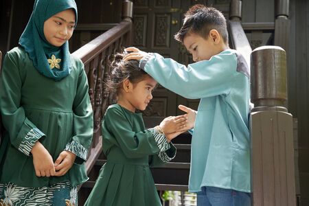 kids in traditional clothing , greeting in front of traditional malay house  during Hari Raya celebration.の写真素材