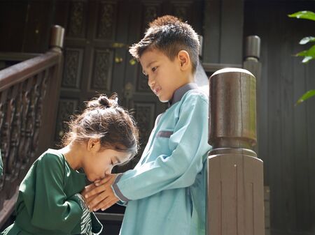 kids in traditional clothing , greeting in front of traditional malay house  during Hari Raya celebration.の写真素材