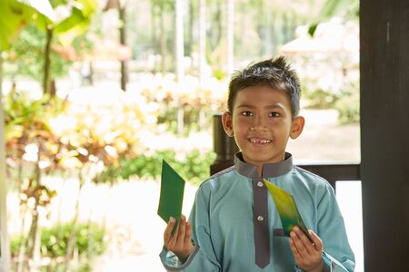 Malay boy with traditional clothing showing his happy reaction after received money pocket during Eid Fitri or Hari Raya celebrationの写真素材