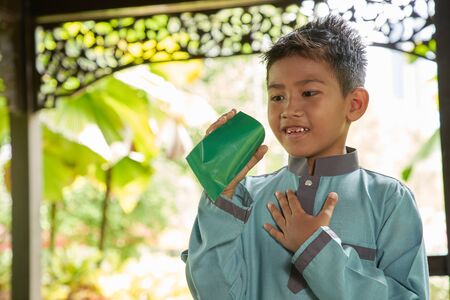 Malay boy with traditional clothing showing his happy reaction after received money pocket during Eid Fitri or Hari Raya celebrationの写真素材