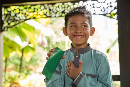 Malay boy with traditional clothing showing his happy reaction after received money pocket during Eid Fitri or Hari Raya celebrationの写真素材