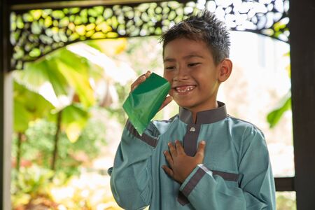 Malay boy with traditional clothing showing his happy reaction after received money pocket during Eid Fitri or Hari Raya celebrationの写真素材