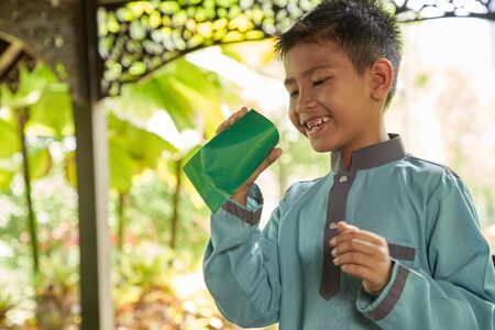 Malay boy with traditional clothing showing his happy reaction after received money pocket during Eid Fitri or Hari Raya celebrationの写真素材