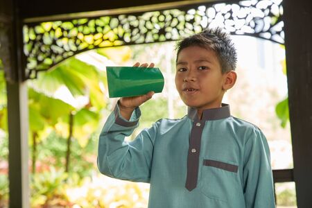 Malay boy with traditional clothing showing his happy reaction after received money pocket during Eid Fitri or Hari Raya celebrationの写真素材