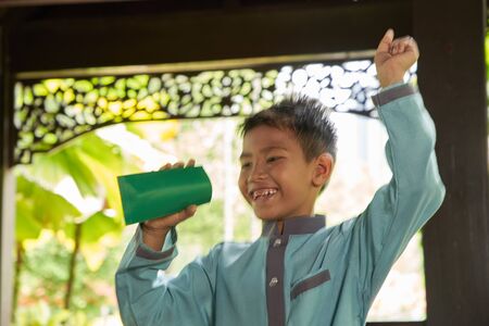 Malay boy with traditional clothing showing his happy reaction after received money pocket during Eid Fitri celebration.slow shutter with some movement to show is is excitedの写真素材