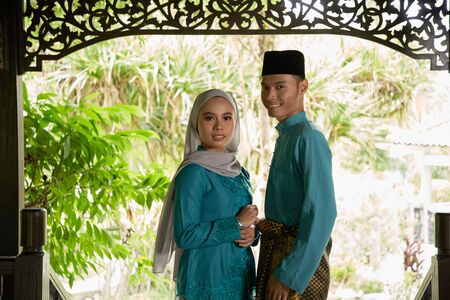 front view of malay couple standing in front of house waiting for visitorsの写真素材