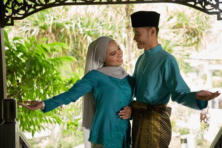 front view of malay couple standing in front of house waiting for visitorsの写真素材