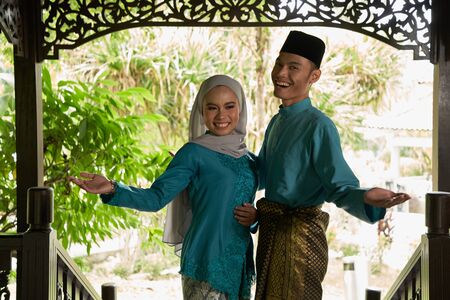front view of malay couple standing in front of house waiting for visitorsの写真素材