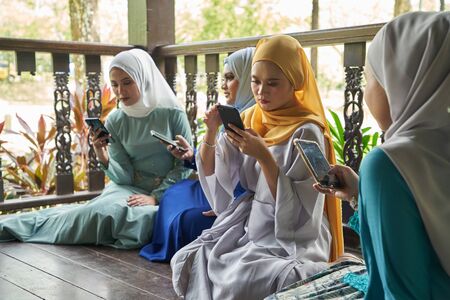 women with traditional clothing using smart phone during ramadan festival celebrationの写真素材