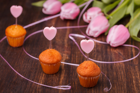 Mini muffin with a candle in the shape of a heart and pink tulips.の写真素材