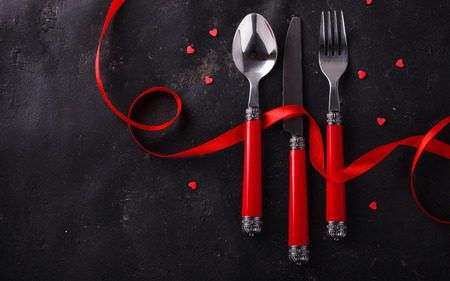 Romantic Valentine's Day celebration, a set of silverware on a dark background,decorated with red ribbon and hearts.selective focusの写真素材