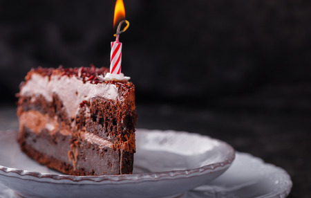 Piece of chocolate cake with candle on a dark background.の写真素材