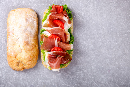 Sandwich with ciabatta, prosciutto,brie cheese and lettuce.On a grey stone background.の写真素材