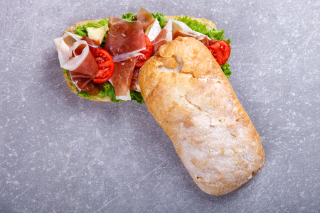 Sandwich with ciabatta, prosciutto,brie cheese and lettuce.On a grey stone background.の写真素材