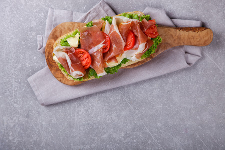 Sandwich with ciabatta, prosciutto,brie cheese and lettuce.on the Board, a grey stone background.の写真素材