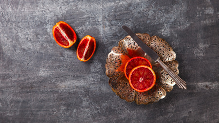 Blood Orange in a metal Plate with a knife on a dark Background.Vintage style.Food or Healthy diet concept.Vegetarian.Copy space for Text. selective focus.の写真素材
