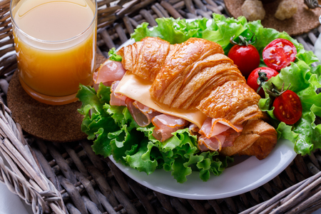 Fresh Croissant Sandwich with  Ham, Cheese,Cherry tomatoes and Salad leaf  on the Tray with Coffee  Milk and a glass of Orange Juice Breakfast in bed Delicious Bakingの写真素材