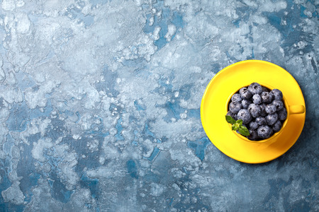 Fresh blueberries in a yellow bright cup and blue background.Concept  Healthy Food. Diet Nutrition .Copy space for Text. Top View. Flat Lay.selective focus.の写真素材