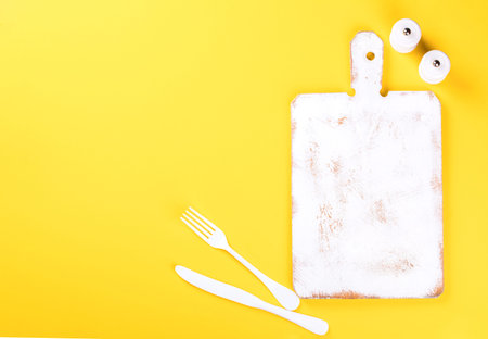 Kitchen chopping wooden board of white color on a bright yellow background. Concept of cooking....