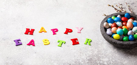 Easter holiday concept.Painted eggs in a plate on a gray background. Holiday decorative willow...