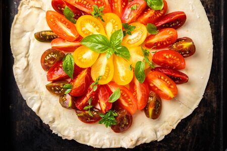 Summer cake with cherry tomatoes, brie cheese and basil. Baking dough with vegetables, greens.の写真素材