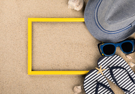 Yellow photo frame and Beach accessories.Beach sand background. Summer time vacation concept. Flat...