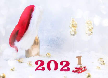 New Year's festive card with numbers 2021. Composition Champagne bottle in Santa Claus hat with glasses and traditional decorations.Light winter background.Light Effect Bokeの写真素材