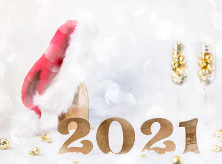 New Year's festive card with numbers 2021. Composition Champagne bottle in Santa Claus hat with glasses and traditional decorations.Light winter background.Light Effect Bokeの写真素材