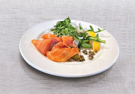 Salmon Carpaccio with arugula, lemon, pickled cucumber and capers on white plateの写真素材