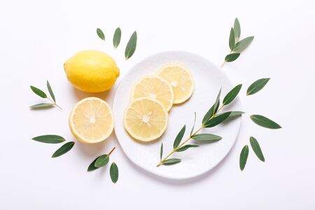 Fresh sliced lemon on plate with green leaves on white backgrounの写真素材