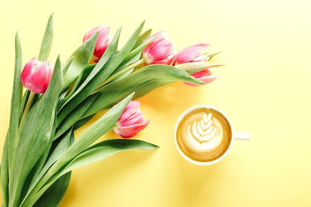 Cup of coffee and pink tulips on yellow background, top viewの写真素材
