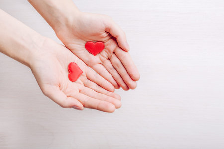 Red hearts in female hands on light background