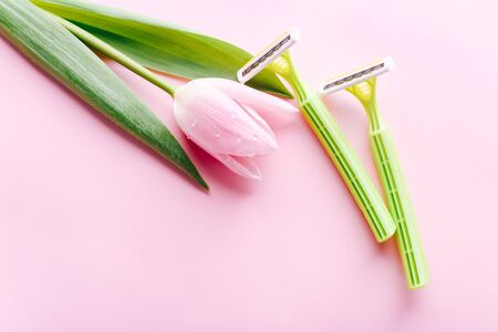 Green razor with beautiful pink tulip on a pink background. Hair removal concept.の写真素材