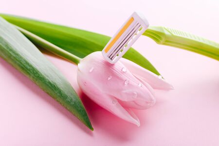 Green razor with beautiful pink tulip on a pink background. Hair removal concept.の写真素材