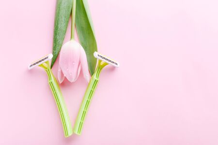 Green razor with beautiful pink tulip on a pink background. Hair removal concept.の写真素材