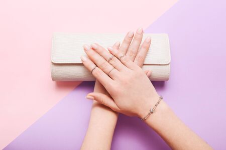Female hand with jewelry and clutch bag on pink and lilac backgroundの写真素材