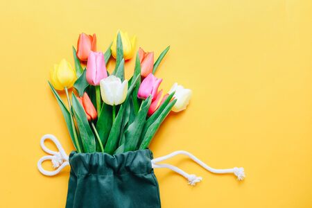 Green eco bag and beautiful color tulips on yellow background. Copy space for your text.の写真素材