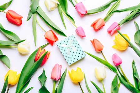 Beautiful tulips and gift box lying on white background, top viewの写真素材