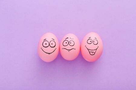 Funny pink eggs with face feeling on purple backgroundの写真素材