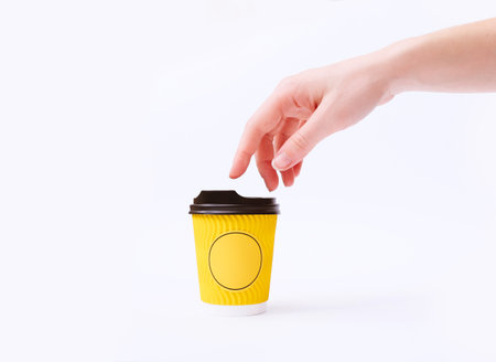 Creative mock up image of woman hand touching yellow paper coffee cup on white background in...