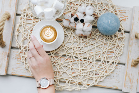 Having a break: female hands holding cup of coffee. Flatlay with candies, candle and flowers