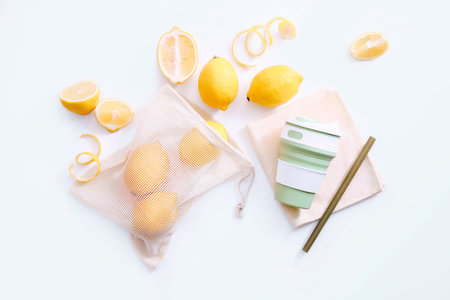 Mesh shopping bag with lemons and reusable cup with straw on white background. Top view. Eco...