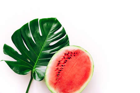 Half of a watermelon on a white background with Monstera leaf.の写真素材
