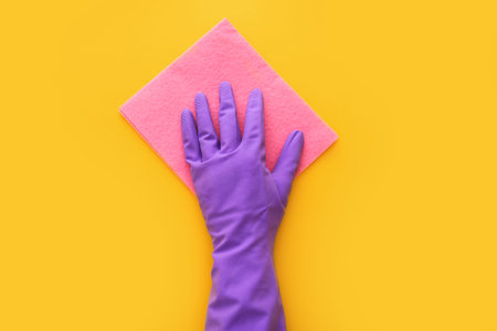 Employee hand in rubber protective glove with micro fiber cloth on yellow background. Spring general or regular clean up. Top viewの写真素材
