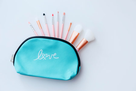 Stylish cosmetic bag with set of brushes on white table background, top view